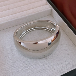Detail of minimalist wide silver bangle showing polished mirror finish and hinge closure