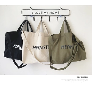Three minimalist canvas tote bags in black, beige, and army green hanging on hooks