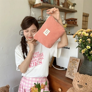 Close-up of pink corduroy makeup bag with embroidered label held by a model