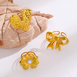Detailed view of three gold bow, heart, and pearl rings on a natural stone surface