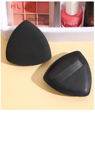 Detail shot of black triangular velvet powder puffs with ribbon handle on beige surface
