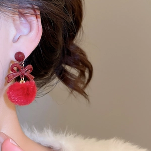 Dettaglio di orecchini con fiocco rosso e pompon di peluche indossati da una modella