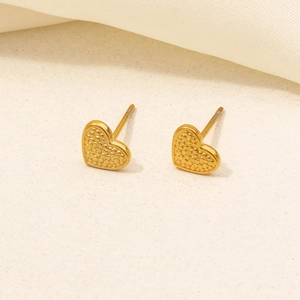 Macro shot of gold heart-shaped stud earrings with fine dotted texture on beige fabric