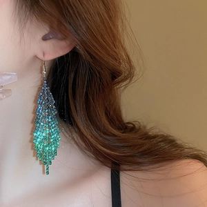 Détail de boucles d'oreilles géométriques à glands avec strass bleu-vert sur modèle