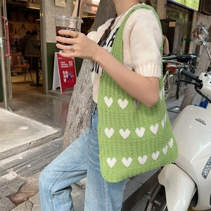 Close-up of green chunky knit tote bag featuring white heart patterns and soft texture