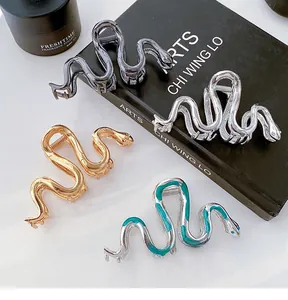 Detailed view of four snake-shaped metal hair claws in gold, silver, black, and green enamel