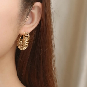 Detailed view of gold spiral hoop earrings with hammered texture on a female model