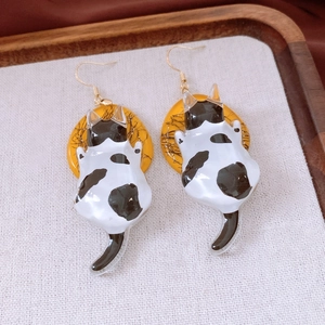 Detailed close-up of cute black and white resin cat pendant earrings on a wooden tray