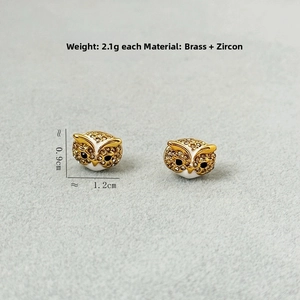 Detailed close-up of owl earrings made of brass with white enamel and zircons