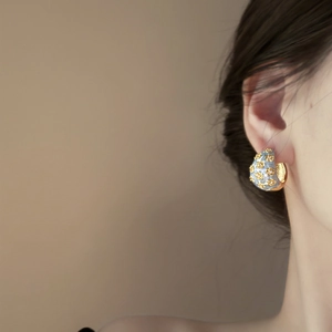 Close-up of vintage C-shape floral enamel earrings worn by a model in soft lighting