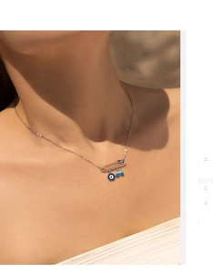 Detail of S925 silver paperclip necklace with evil eye bead and blue car charm on a model