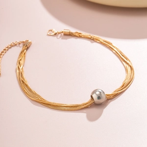 Detail of layered gold chain bracelet with silver spherical bead on peach background