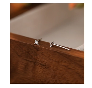 Macro shot of silver four-pointed star earrings with zircon inlay on wood background