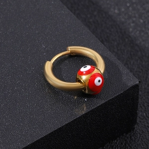 Macro detail of a golden stainless steel hoop earring featuring a red evil eye bead charm