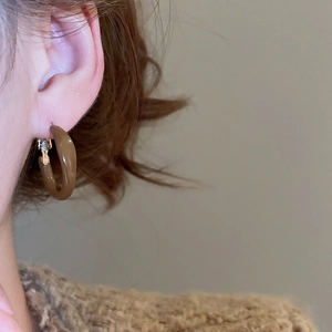 Close-up of amber brown resin C-shape hoop earrings on a model wearing a brown knit sweater