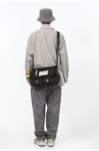 Model back view showing large capacity black messenger bag with dinosaur pendant