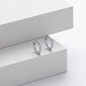 Macro detail of silver S925 sterling silver twisted hoop earrings on white geometric stand