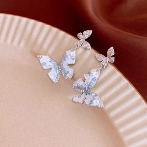 Detailed macro view of silver butterfly earrings with blue crystals on a ceramic tray