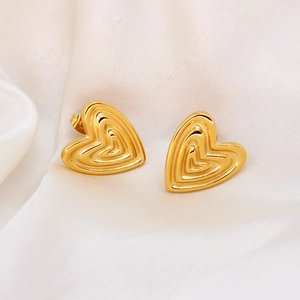 Close-up of golden heart earrings with textured grooves on elegant white silk fabric