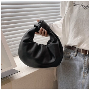 Close-up of black ruched leather handbag featuring a stylish knotted handle design