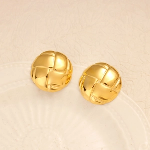 Macro shot of gold grid pattern earrings on a minimalist white ceramic tray