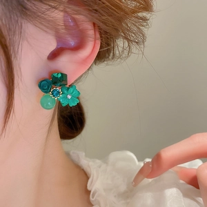 Close-up of green crystal and rose flower stud earrings worn on a model's ear