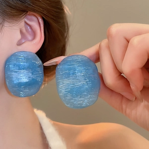 Detail showing blue resin earrings with brushed texture on female model's ear