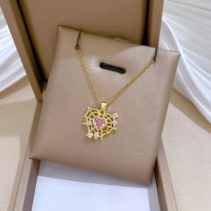 Macro view of gold heart necklace with pink gem and spiderweb design in a gift box