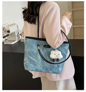 Detail of blue denim tote bag with black strap and white cloud plush charm on a model