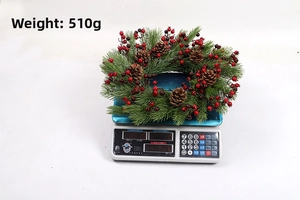 Christmas wreath with red berries and pine cones weighed on scale, 510g net weight