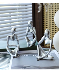 Close-up of three silver thinker sculptures in modern abstract style on books