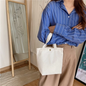 Detail view of white canvas lunch bag with bronze metal clasp held by a model in casual setting