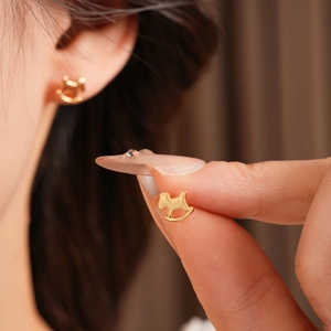 Détail de boucles d'oreilles cheval à bascule plaquées or portées et tenues en main