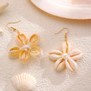 Dettaglio di orecchini a fiore di conchiglia con perle e ganci dorati su decoro