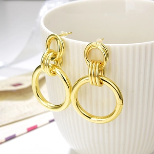 Detailed view of golden triple hoop earrings hanging on a white textured ceramic cup