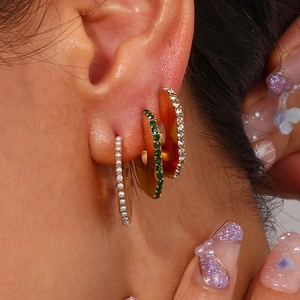Detail of stacked gold hoop earrings with green zircon and pearl on model's ear