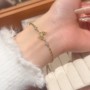 Detailed view of an 18k gold butterfly bracelet with zircons on a white plush cuff