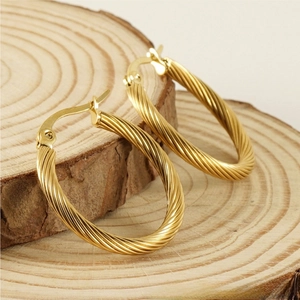 Macro detail of gold-plated twisted rope hoop earrings on natural wood texture background