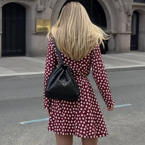 Rear view of wine red polka dot dress with long sleeves and black drawstring backpack