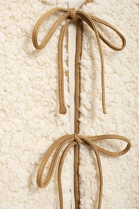 Detail of cream sherpa fleece vest with brown suede tie-up closures and soft texture