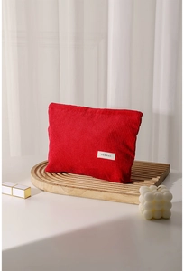 Detail view of red corduroy makeup bag with small white label on a wooden tray