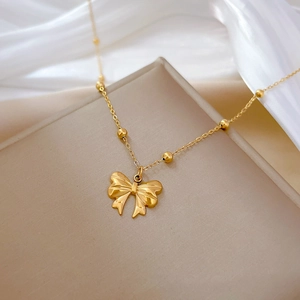Close-up of a gold bow pendant necklace with bead chain on silk background