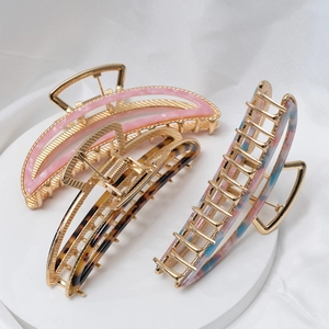 Three metal shark hair clips with tortoiseshell and marble acetate patterns on a white stand