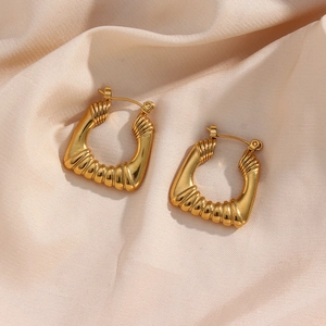Macro detail of gold geometric earrings with spiral texture on soft beige silk