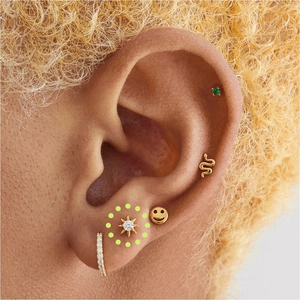 Close-up of gold starburst, snake, and emerald studs with pavé hoops on ear cartilage