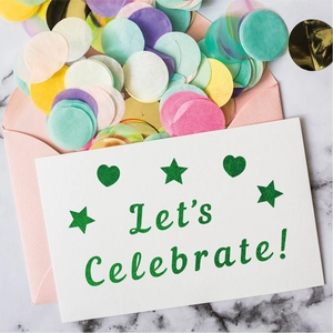 Flat lay of Let's Celebrate greeting card with pink envelope and pastel confetti