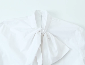 Detailed view of the white blouse collar with elegant bow tie and back button closure