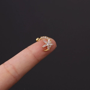 Detailed macro view of a gold moon and star cartilage stud earring held by hand