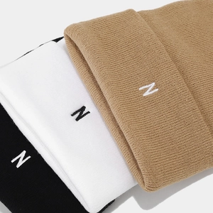 Detail shot of the knit texture and N embroidery on black, white, and khaki beanies