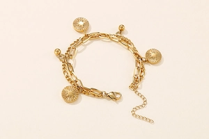 Detail of double-layer gold titanium steel bracelet featuring sunburst engraved coin pendants